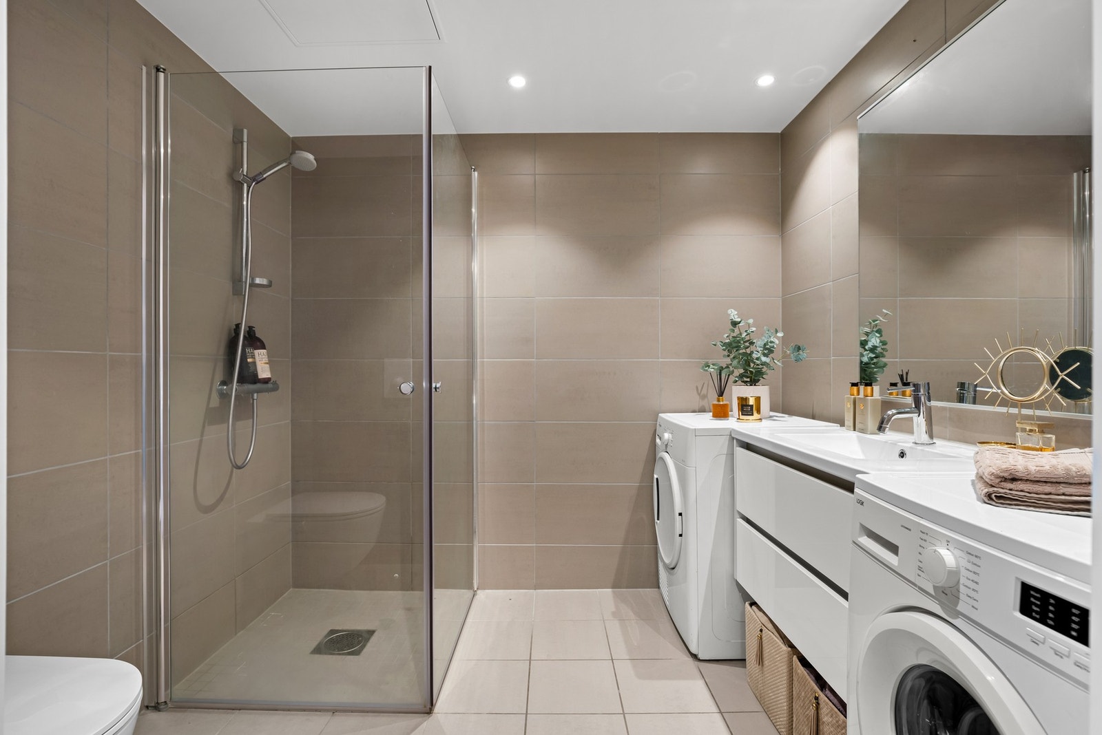 Dusjhjørne med skyvbare glassdører og vegghengt toalett. Servant med skuffløsninger under for toalettsaker, håndklær og diverse. Galleribilde