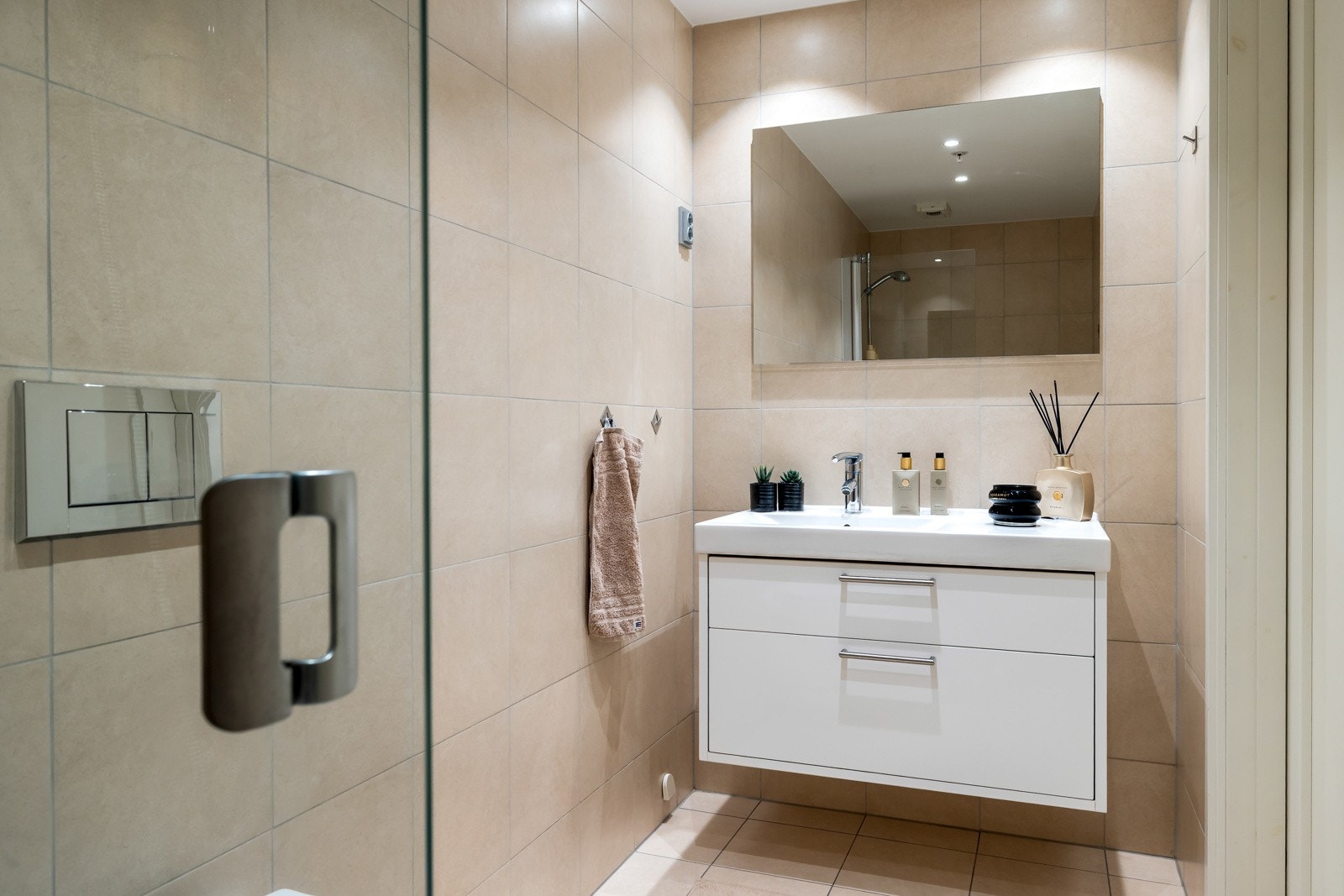 Det andre badet ligger praktisk til ved entreen, og er holdt i samme farge- og materialkombinasjon som hovedbadet. Baderomsinnredningen har heldekkende servant med skuffeløsning, og over er det både speil og stikkontakt. Galleribilde