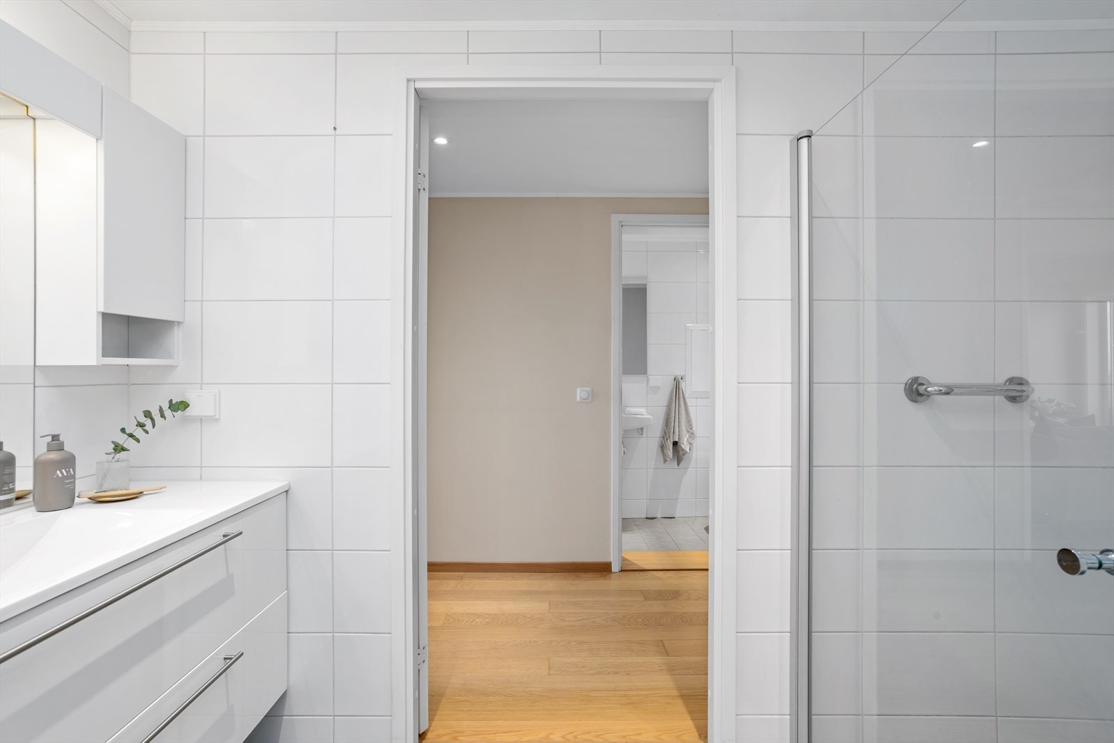 Veggene har tidsriktige, rektangulære veggfliser mens det på gulvet er valgt en gråtonet farge for å skape en matchende kontrast. Baderommet har innfelte downlights med nivåjustering i himling. Galleribilde