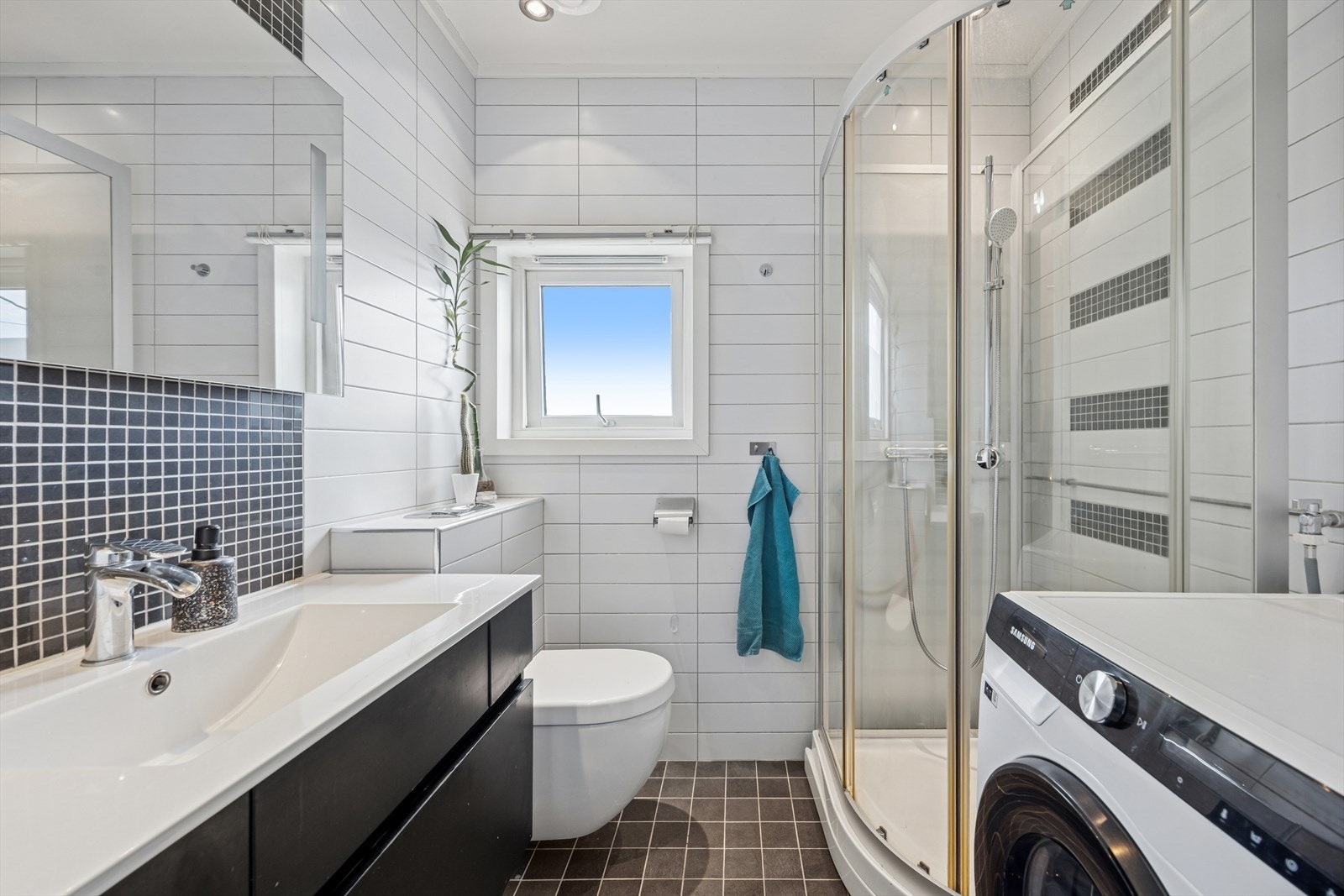 Flislagt bad med elektriske varmekabler beliggende i huset 2. etasje, utstyrt med vegghengt toalett, dusjkabinett, samt baderomsinnredning med servant og opplegg for vaskemaskin. Galleribilde