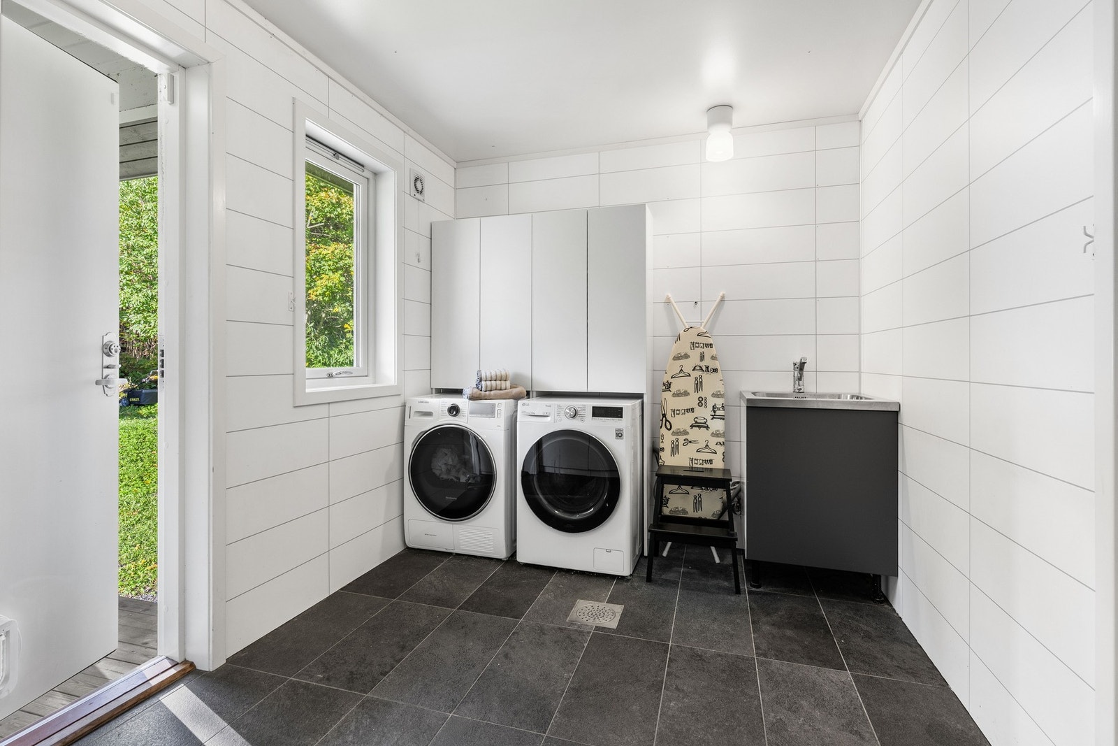 Vaskerommet er innredet med en utslagsvask, skap og opplegg til vaskemaskin og tørketrommel. Det er også en praktisk dør ut. Galleribilde