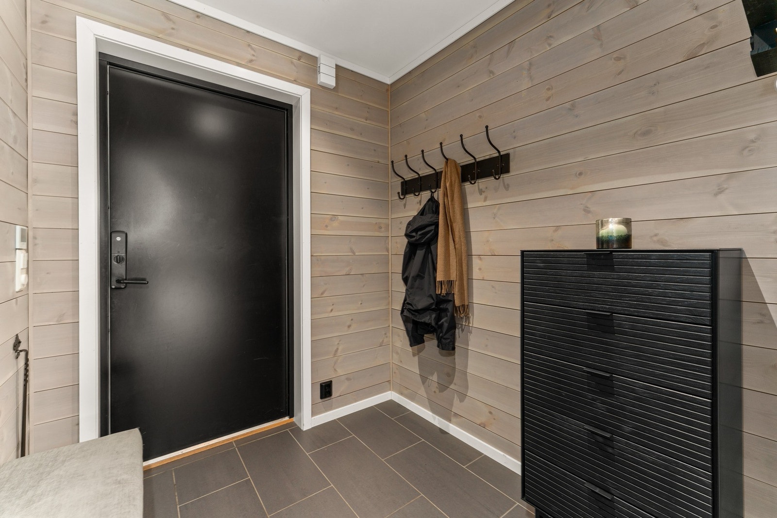 Inngangspartiet gir et solid førsteinntrykk med mørkgrå fliser, beisede panelvegger og elegant spotbelysning. Galleribilde