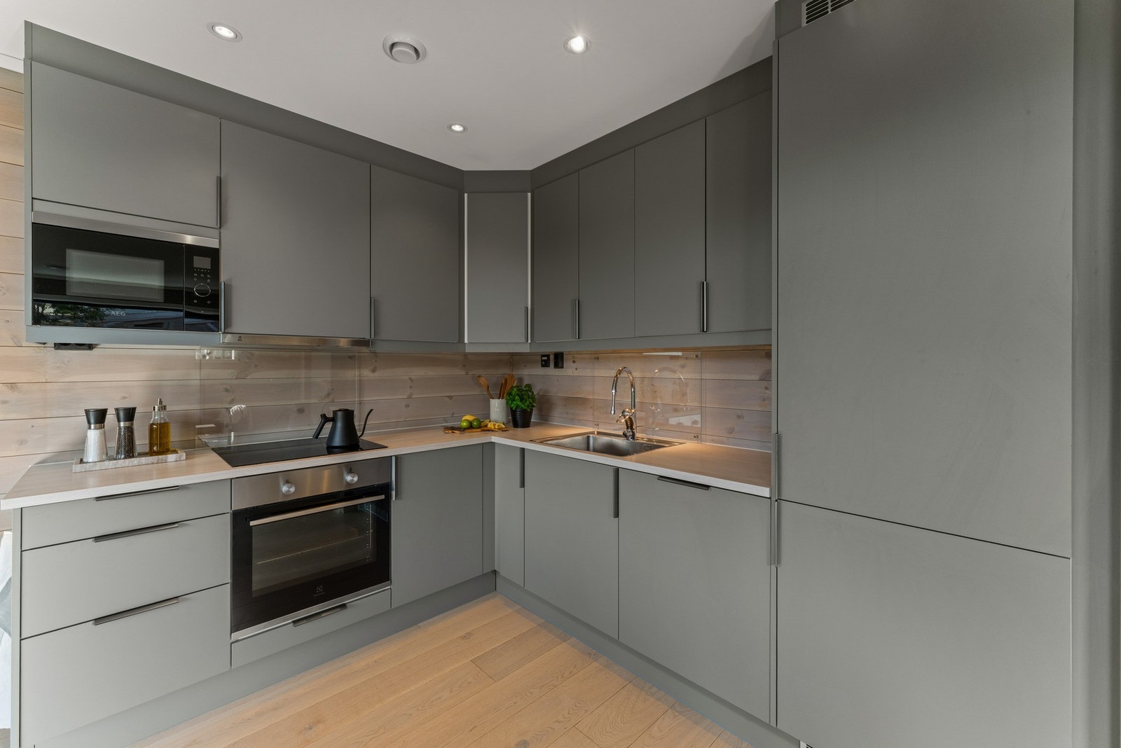 Kjøkkenet har et moderne og tidløst uttrykk med glatte grå fronter, integrerte hvitevarer og belysning under overskapene som gir et elegant og funksjonelt arbeidslys. Galleribilde