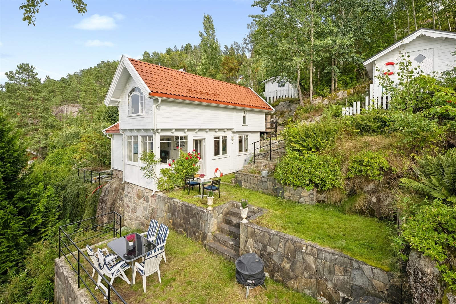 Sjarmerende fritidseiendom med flere uteplasser, fine utsiktspunkter, terrasser i naturstein og frodige omgivelser. Nyt rolige dager i solen med flott sjøutsikt. Galleribilde