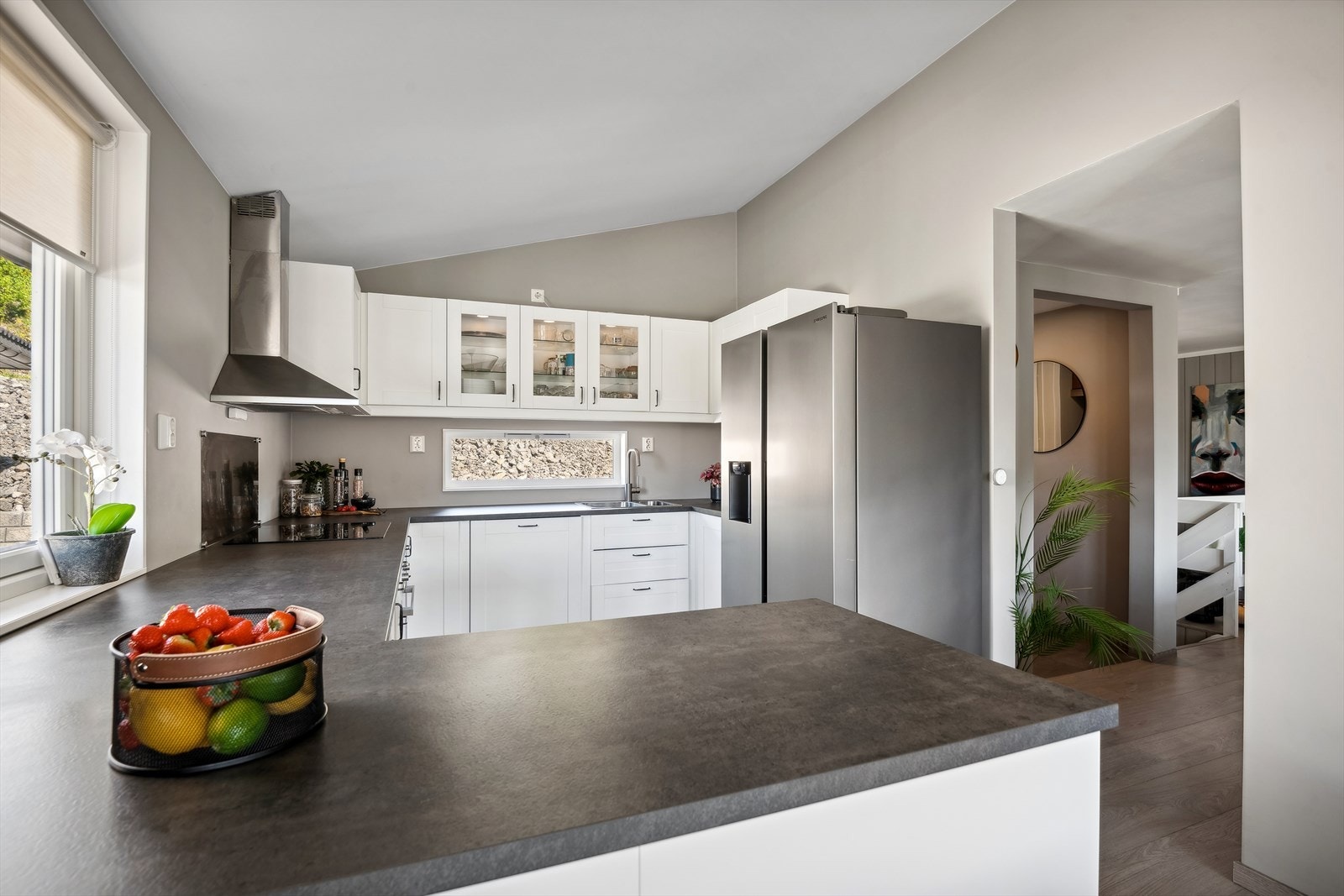 Pen og stilren kjøkkeninnredning fra 2021 med profilerte, hvite fronter og mørk laminat benkeplate med nedfelt vaskekum og induksjonstopp. Galleribilde