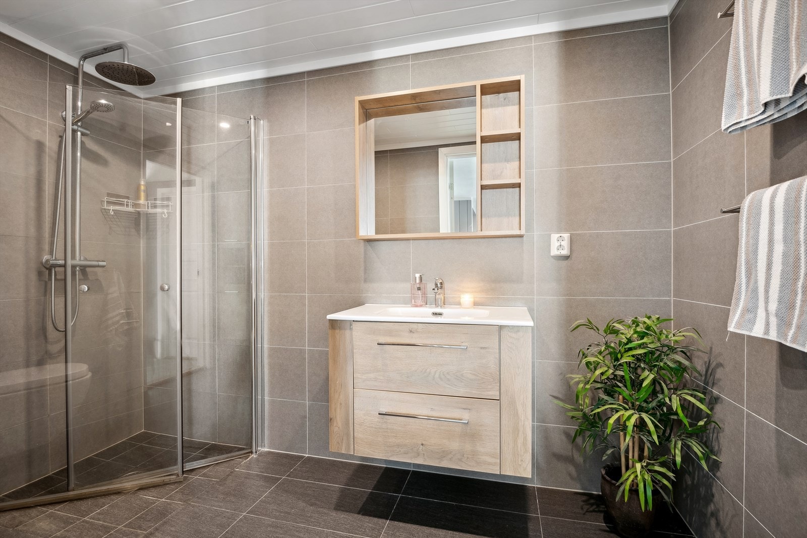 Dusjområdet har glassdører i herdet glass som kan felles inn, samt et veggmontert dusjsett med både regn- og hånddusj. Galleribilde