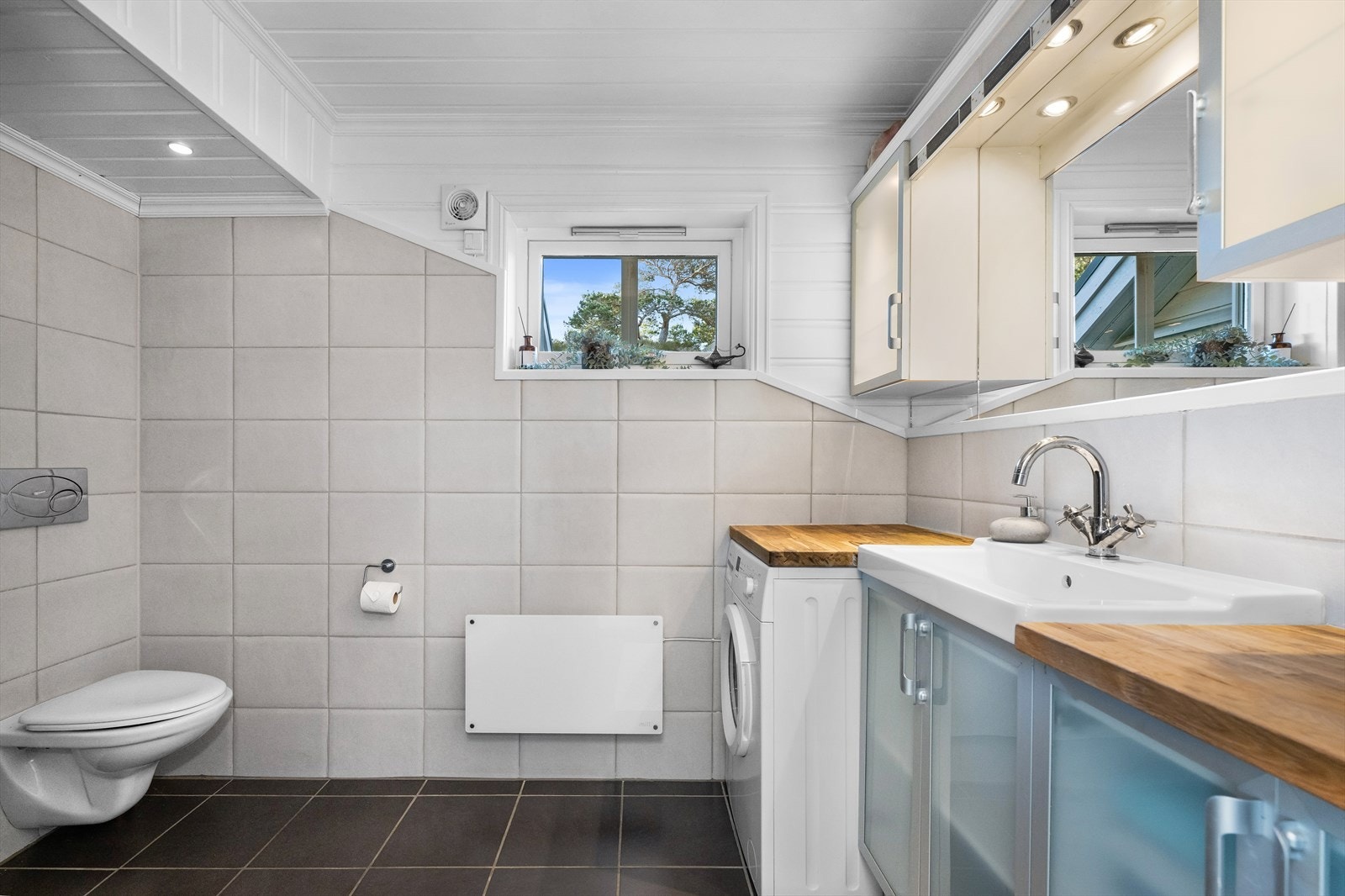 Badet er helfliset og pent, og har innredning som vegghengt klosett, dusjkabinett og servantinnredning med skap og veggskap. Galleribilde