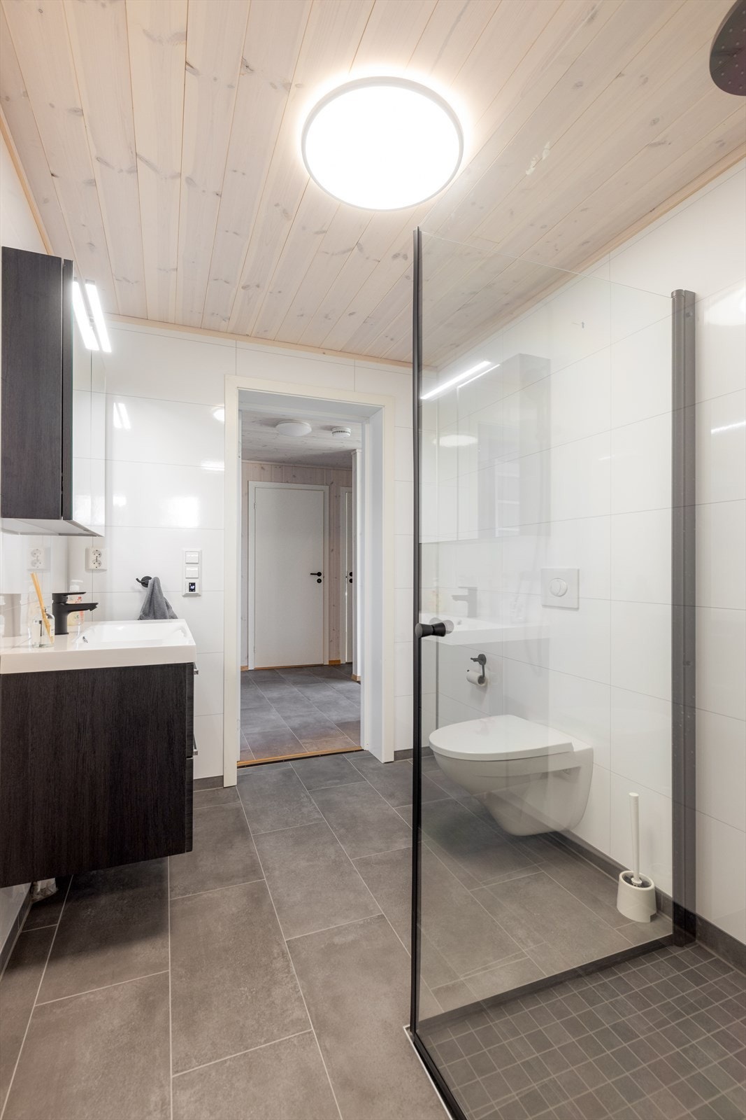 Badet inneholder dusjhjørne, veggmontert toalett og servantinnredning med skuffer og speilskap med overlys. Galleribilde