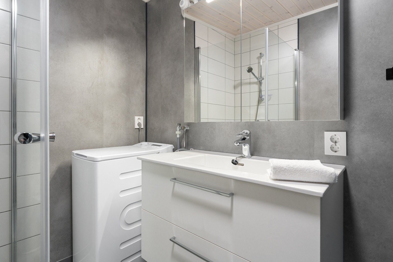 Badet er utstyrt med vegghengt servant med oppbevaringsplass, dusjhjørne med innfellbare vegger og opplegg til vaskmaskin.