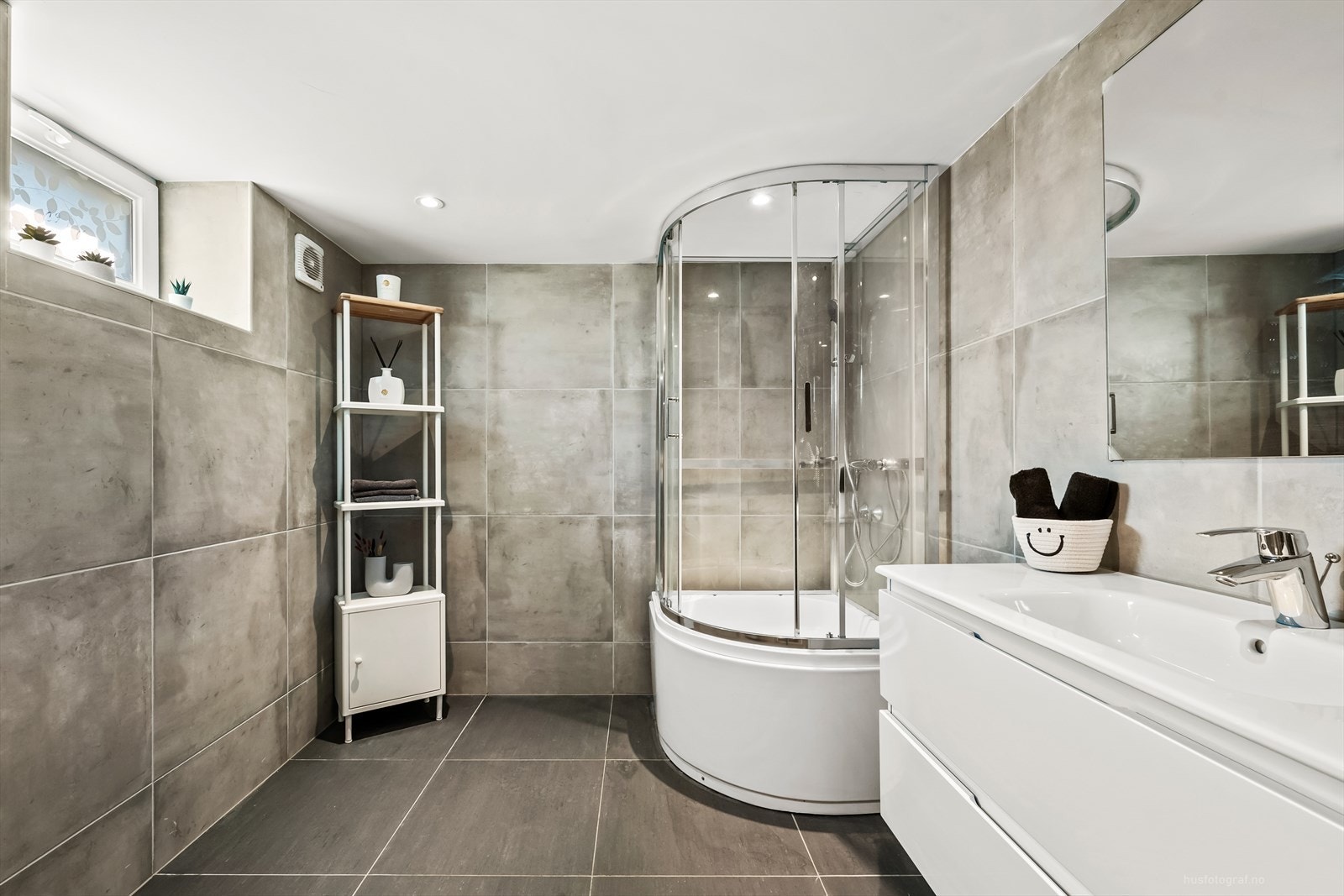 Hovedbadet i underetasjen er innredet med hvit baderomsinnredning, speil og rom for oppbevaring i skuffeseksjon. Galleribilde