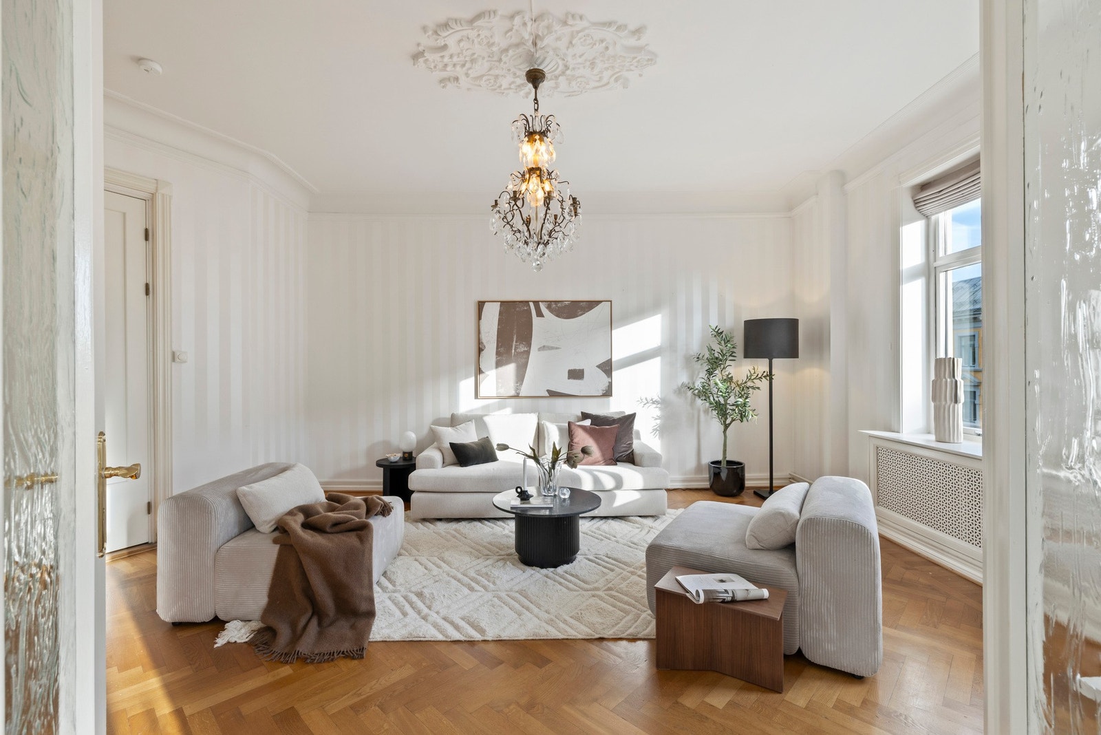 Begge stuene er smakfullt innredet med fiskebensparkett, nydelige takrosetter og hvite vegger for et delikat uttrykk.