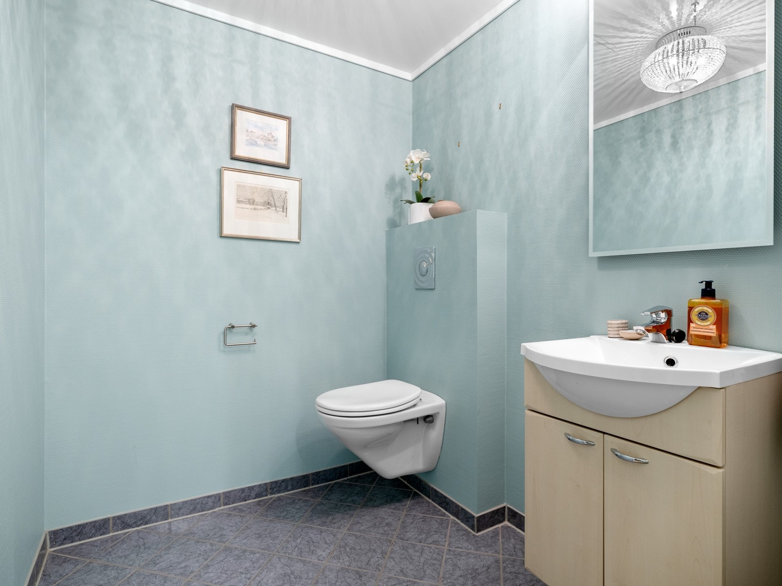 Gjestetoalettet ligger i praktisk tilknytning til entreen og er innredet med fliser på gulv med gulvvarme og malte veggflater. Innredningen består av en nedfelt servant på skuffeseksjon, speil og veggmontert toalett. Galleribilde