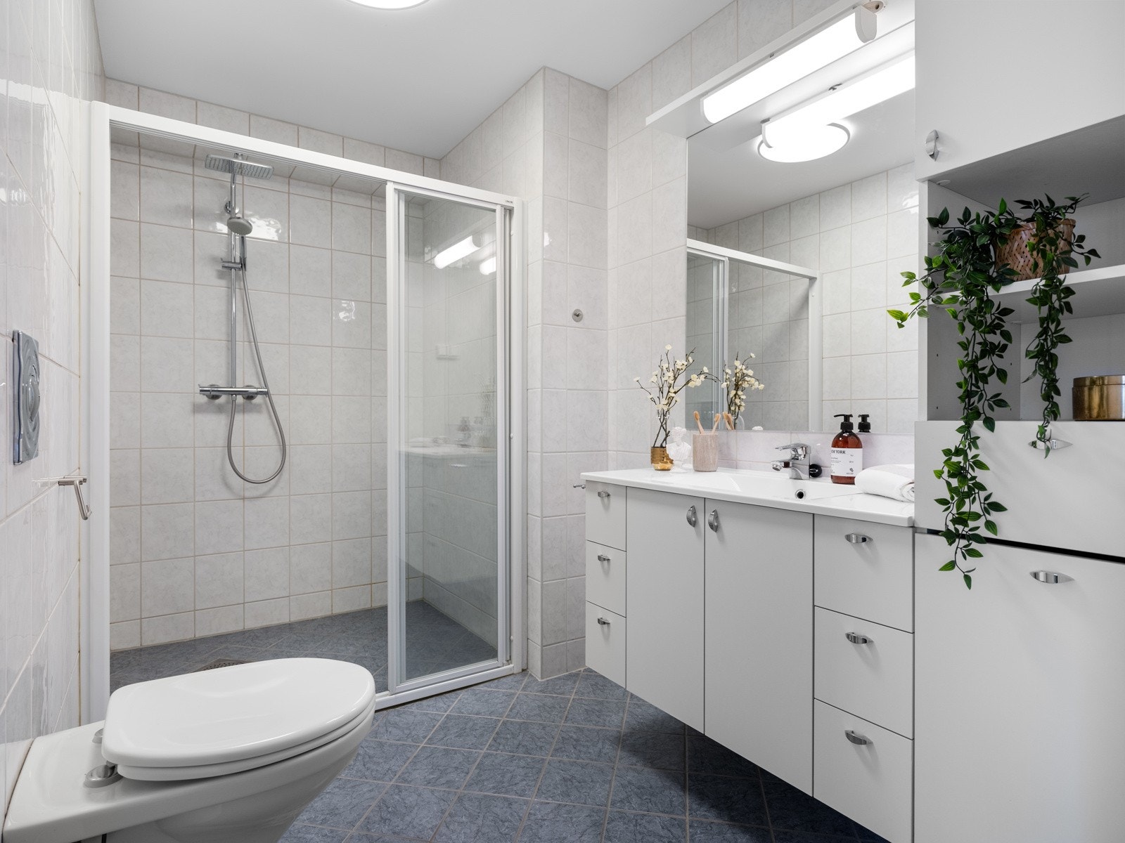 Badet i tilknytning til hovedsoverommet og er helfliset, det er såklart gulvvarme. Innredningen består av servant på en hvit skap- og skuffeseksjon, høyskap og speil med overhengende belysning. Videre er badet utstyrt med toalett og regnfalldusj. Galleribilde