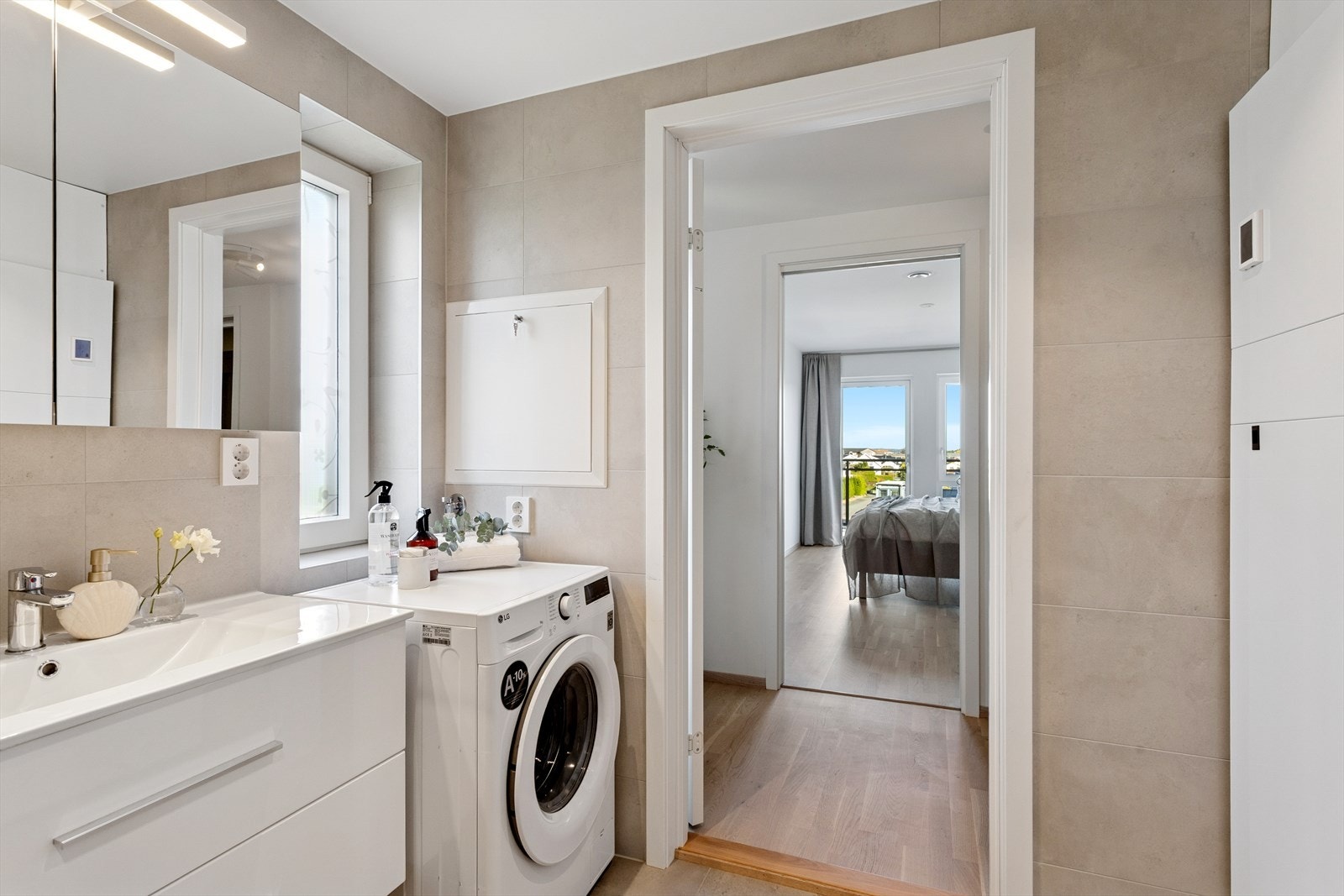 Baderomsinnredningen har doble kolonialskuffer og helstøpt servantbenk. Overskap med speildører og lysarmatur av LED forsterker det moderne og innovative. Til sides for baderomsinnredningen, er det ferdig opplegg for vaskemaskin. Galleribilde