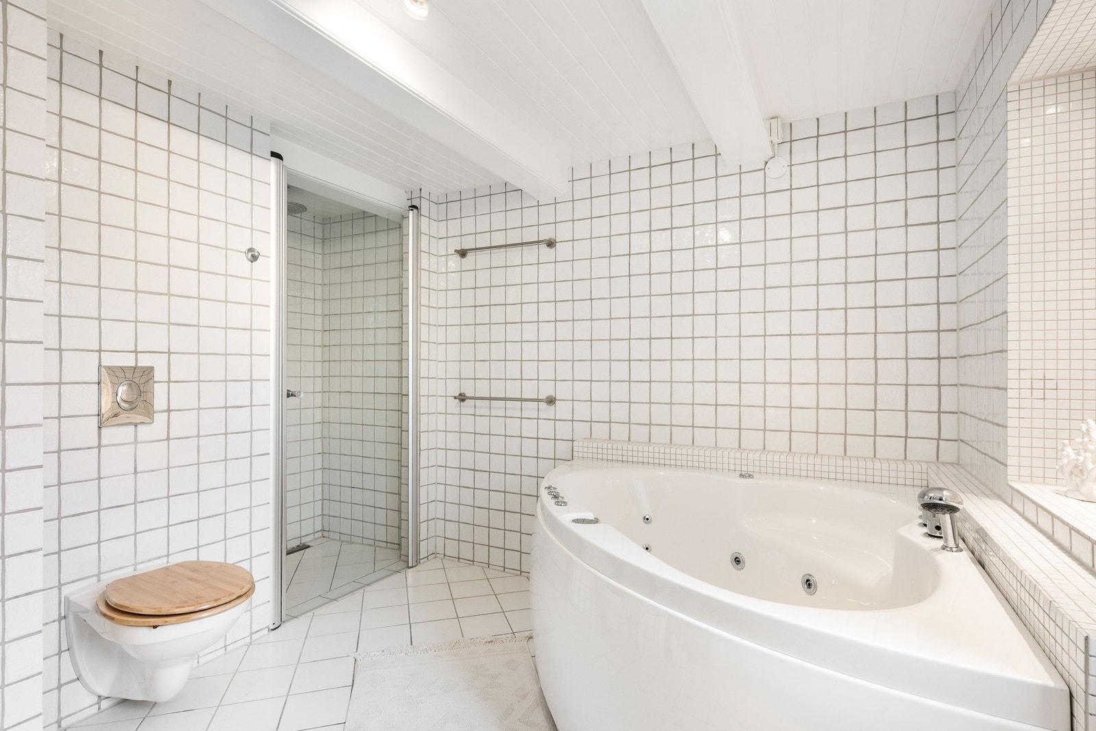 Bad med dusj, hjørnebadekar, toalett og nedfelt servant med innredning. Galleribilde