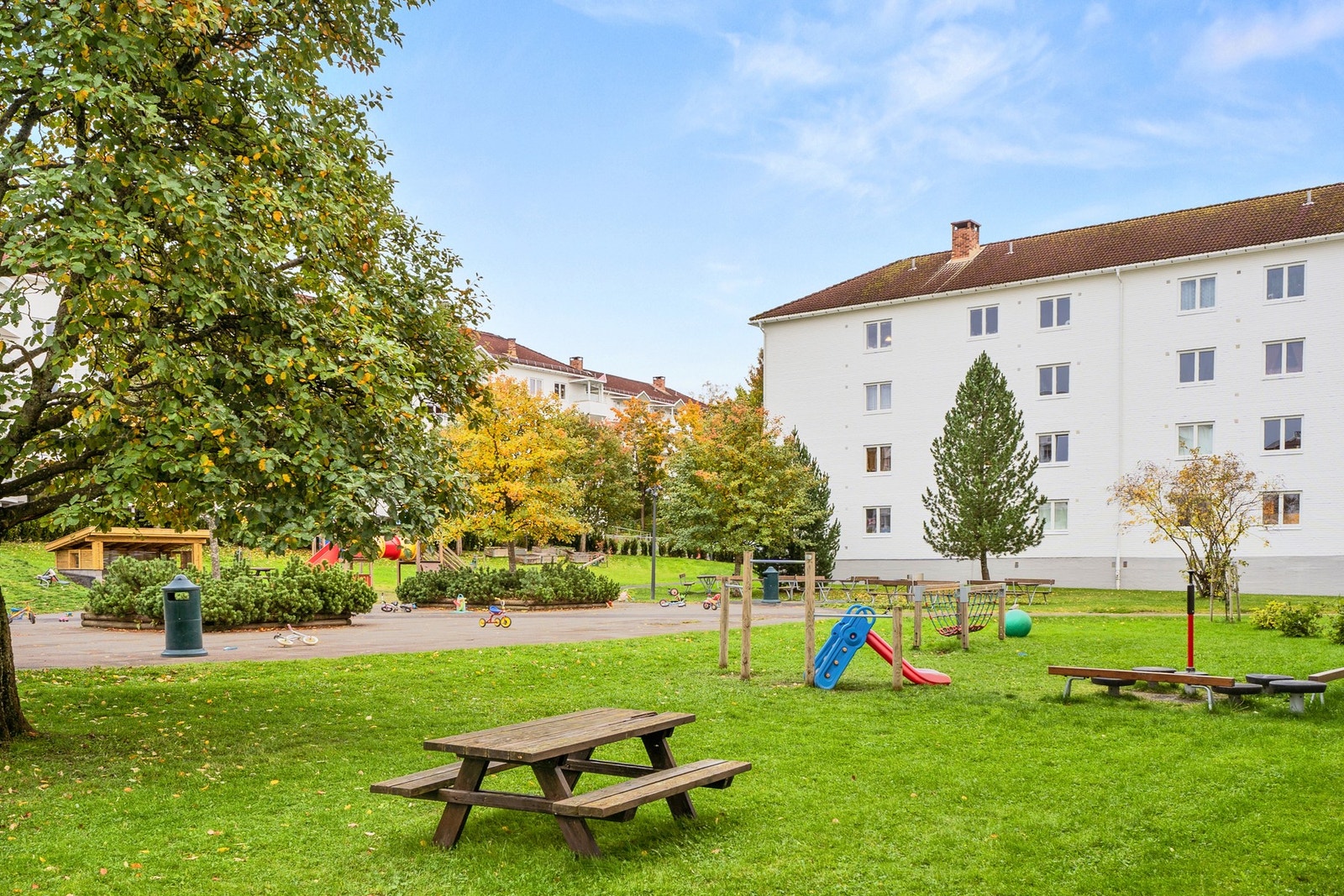Fellestomten er grønn og solrik, med boltreplass, lekeapparater og sittebenker. Galleribilde