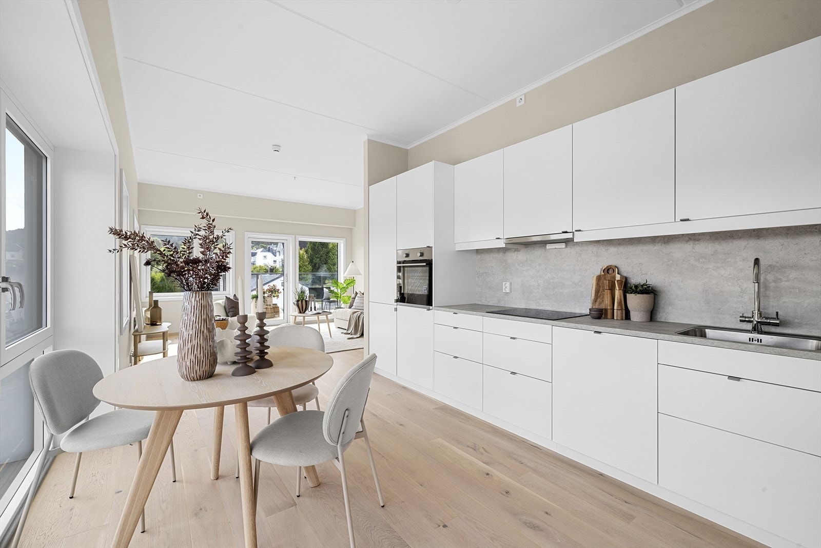 Tidløst kjøkken med hvite, slette fronter og laminert benkeplate. Innredningen har integrert oppvaskmaskin, stekeovn, platetopp og kjøl/fryseskap Galleribilde