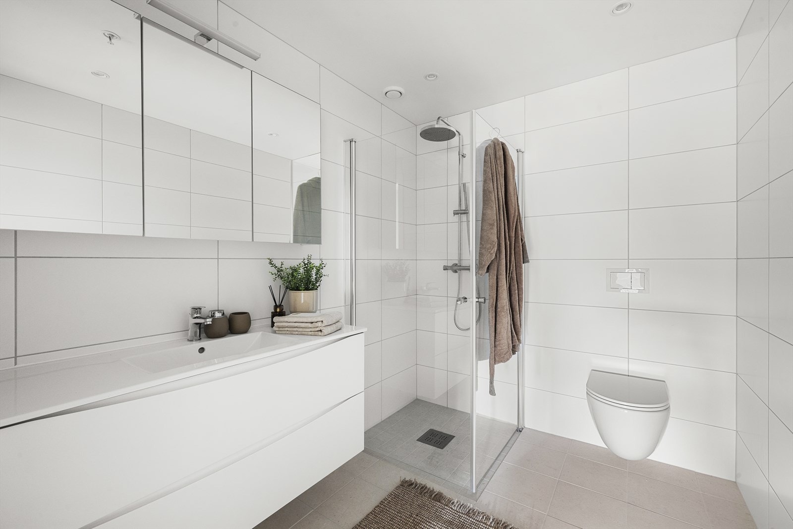 Stilrent helfliset baderom med gulvvarme. Badet er utstyrt med vegghengt toalett og dusjhjørne med innfellbare glassvegger Galleribilde