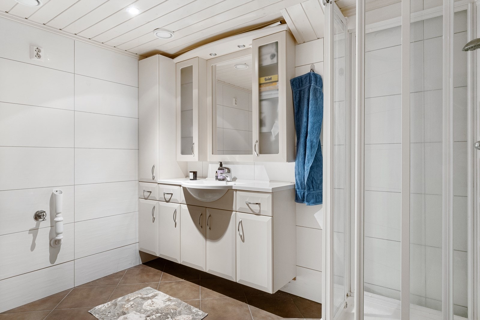 Baderommet i underetasjen har fliser på gulv/vegger og malt trepanel med downlights i himling. Galleribilde