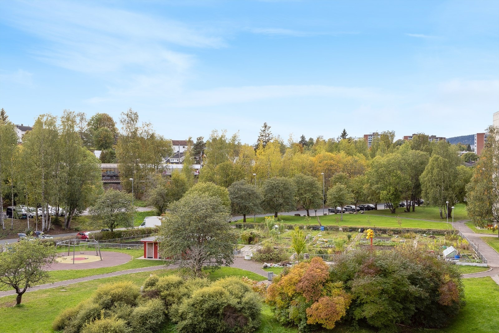 Utsikt fra leiligheten mot grønt fellesområde med lekeplass og frodig beplantning. Rolig og barnevennlig beliggenhet med kort vei til tog, skole og senter. Galleribilde
