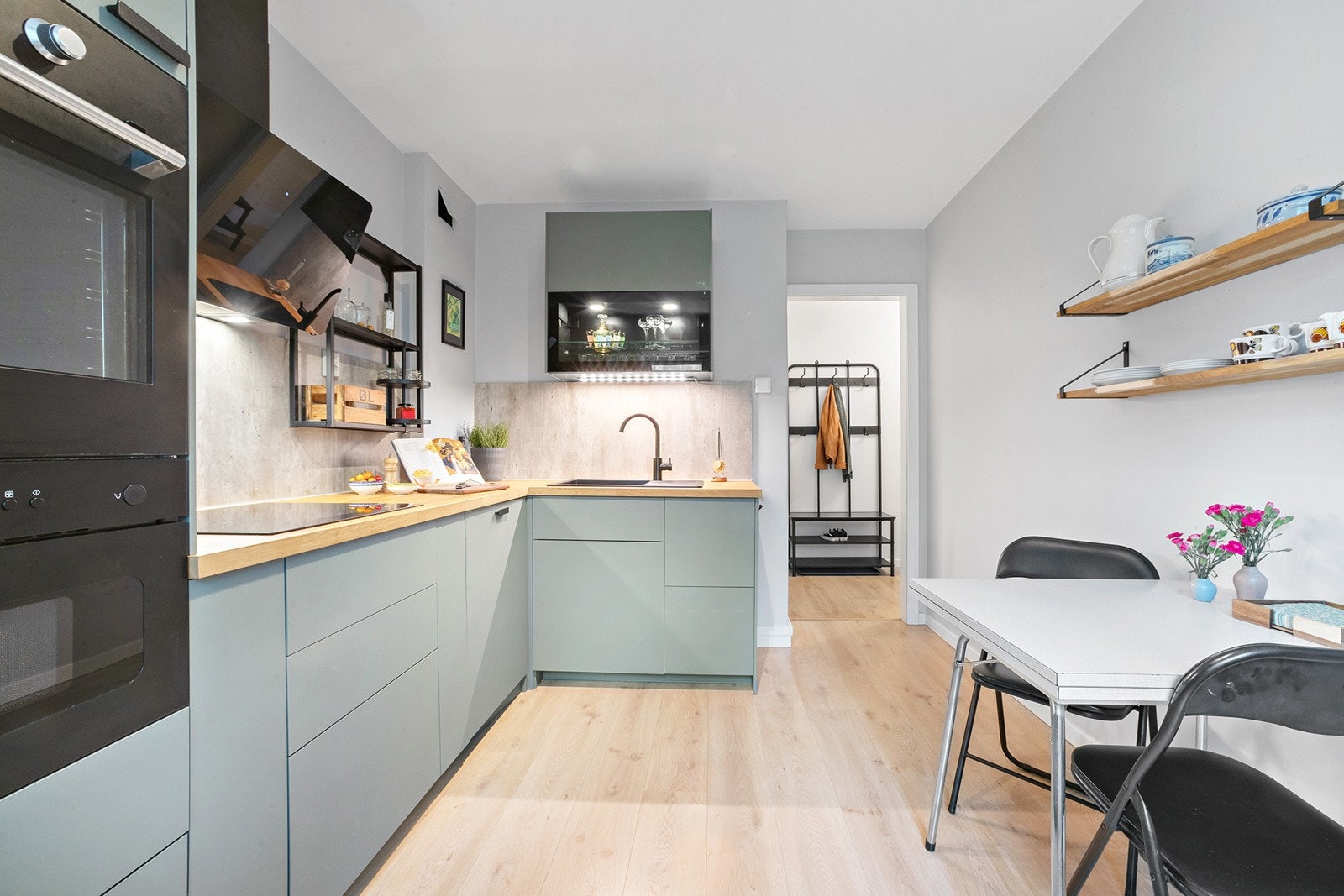 Moderne IKEA-kjøkkeninnredning med glatte folierte skapfronter, heltre benkeplate med sprutplate på bakvegg, enkel oppvaskkum med benkebeslag, ventilator og integrerte hvitevarer som koketopp, stekeovn, mikrobølgeovn, oppvaskmaskin, kjøl/- fryseskap. Galleribilde