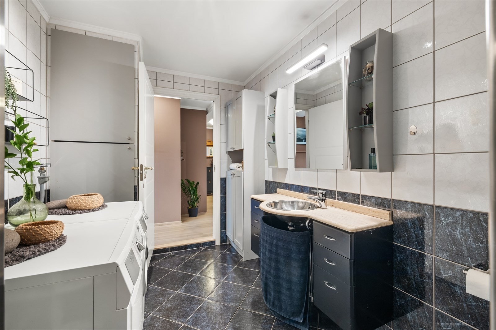 Det er plassbygget skap som skjuler varmtvannsbereder og avtrekksaggregat. Det er dusjnisje med glassbyggerstein, gulvstående toalett og opplegg til vaskemaskin. Galleribilde