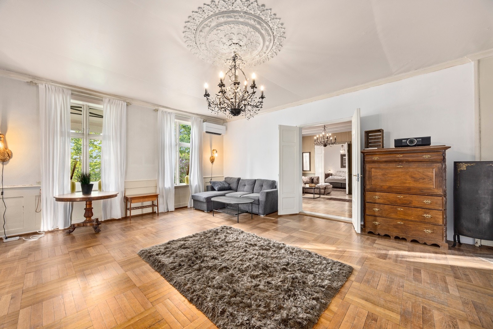 Lys og romslig stue med dekorativ takrosett og varmepumpe installert i 2023. Rommets størrelse og utforming gjør det mulig å etablere en kjøkkenløsning, noe som vil gjøre leiligheten komplett og ideell for utleie. Galleribilde