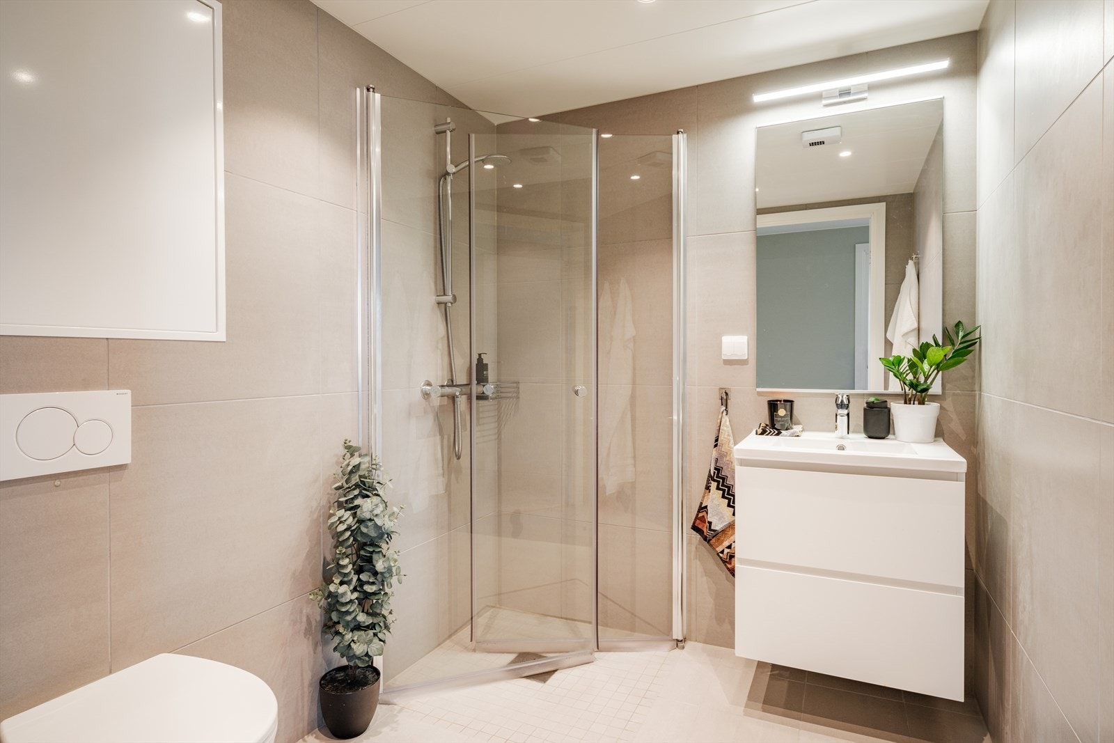 Flislagt med gulvvarme, servantskap med glatte fronter og heldekkende servant, speil og lysarmatur, dusjhjørne med svingdører og håndholdt dusj, samt veggmontert toalett. Galleribilde