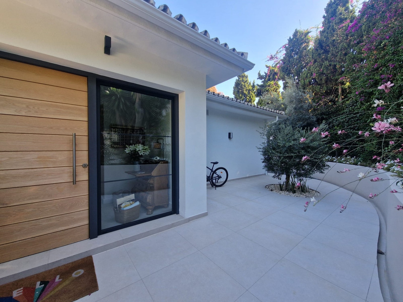 En spesialtilpasset bred inngangsdør og et imponerende vindu gir et slående førsteinntrykk når du kommer inn i Casa Salma, en moderne villa i Marbella designet for elegant kystliv.
A bespoke wide front door and statement picture window create a striking f Galleribilde