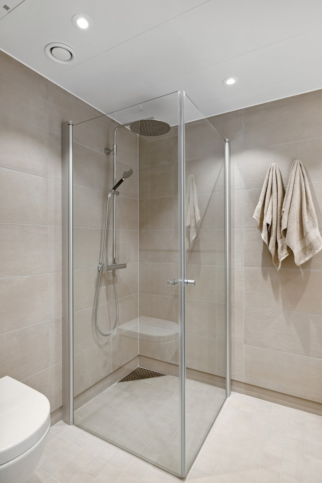 Begge badene er utstyrt med regnfallsdusj og fliser i "Sand" (beige) Galleribilde