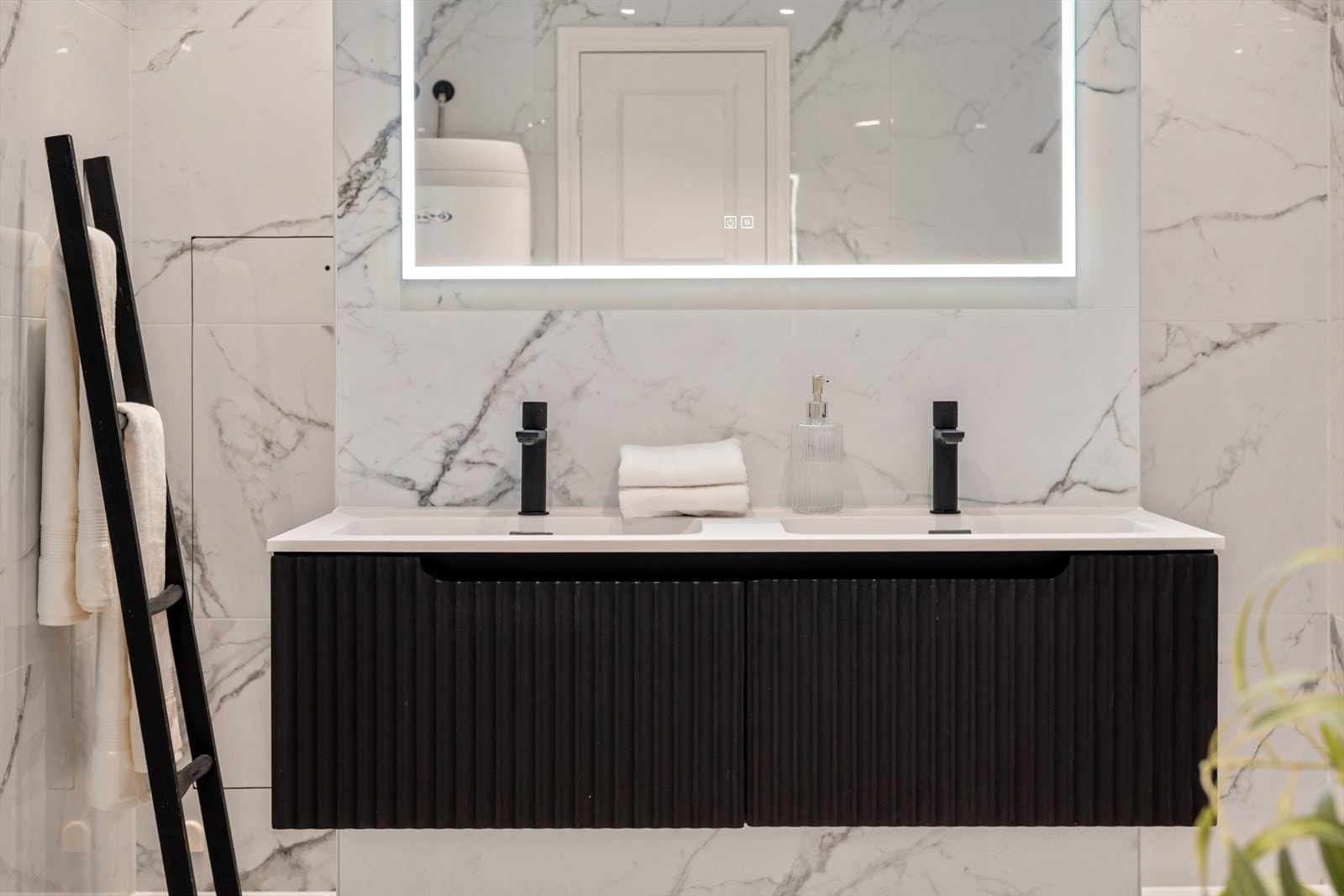 Badet er innredet med dobbel servant i skuffeinnredning, speil med integrert belysning, massasjebadekar, dobbelt dusj og vegghengt toalett. Galleribilde
