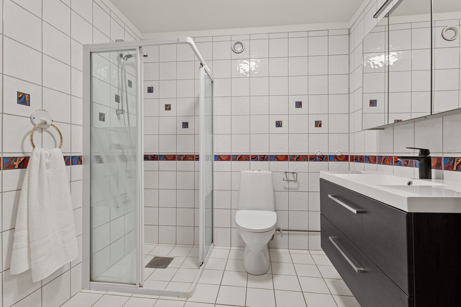 Baderommet er innredet med gulvstående toalett, dusjhjørne og servant med underskuffer som gir god oppbevaringsplass. Galleribilde