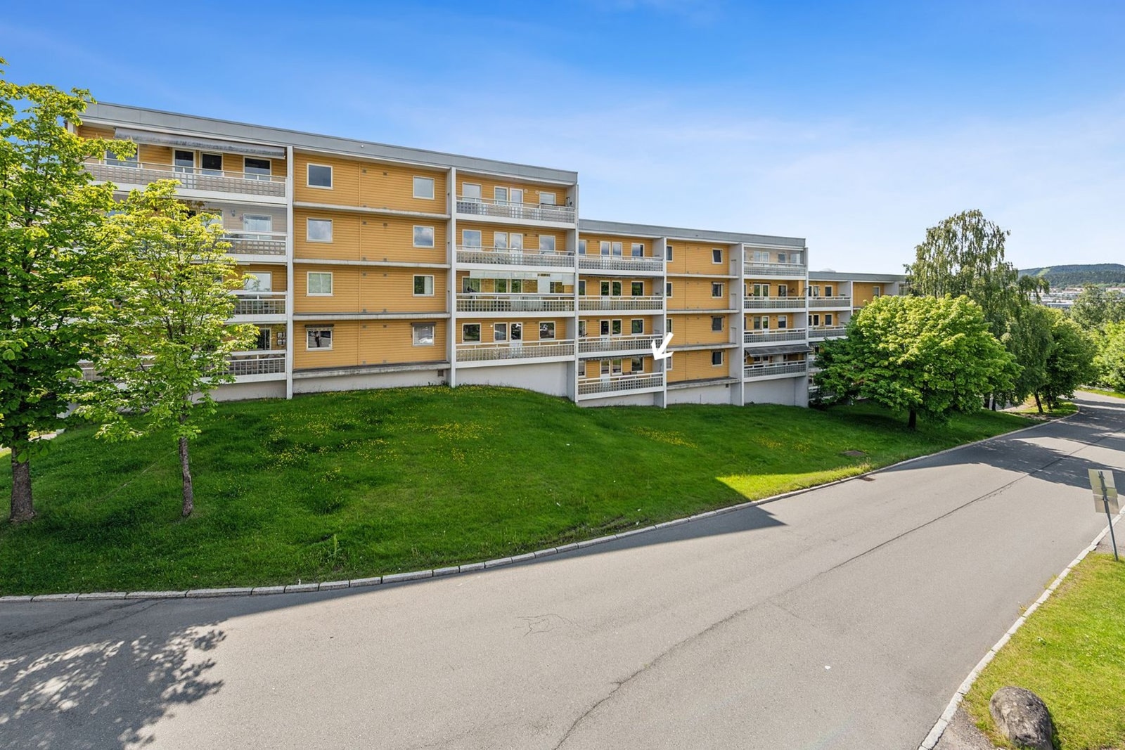 Fasade vist fra terrasse på kjøkkensiden, hvor leiligheten ligger i skrånet terreng og fremstår som en høy 1. etasje. Galleribilde