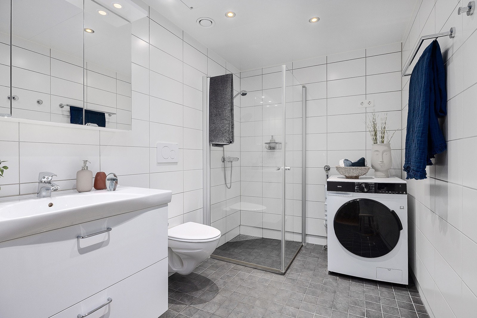 Pent flislagt bad med varme i gulv. Det er servant med skuffeseksjon og overskap med lys. Videre er det vegghengt toalett og dusjhjørnet med svingbare skyvedører i glass. Badet har opplegg for vaskemaskin og tørketrommel. Galleribilde
