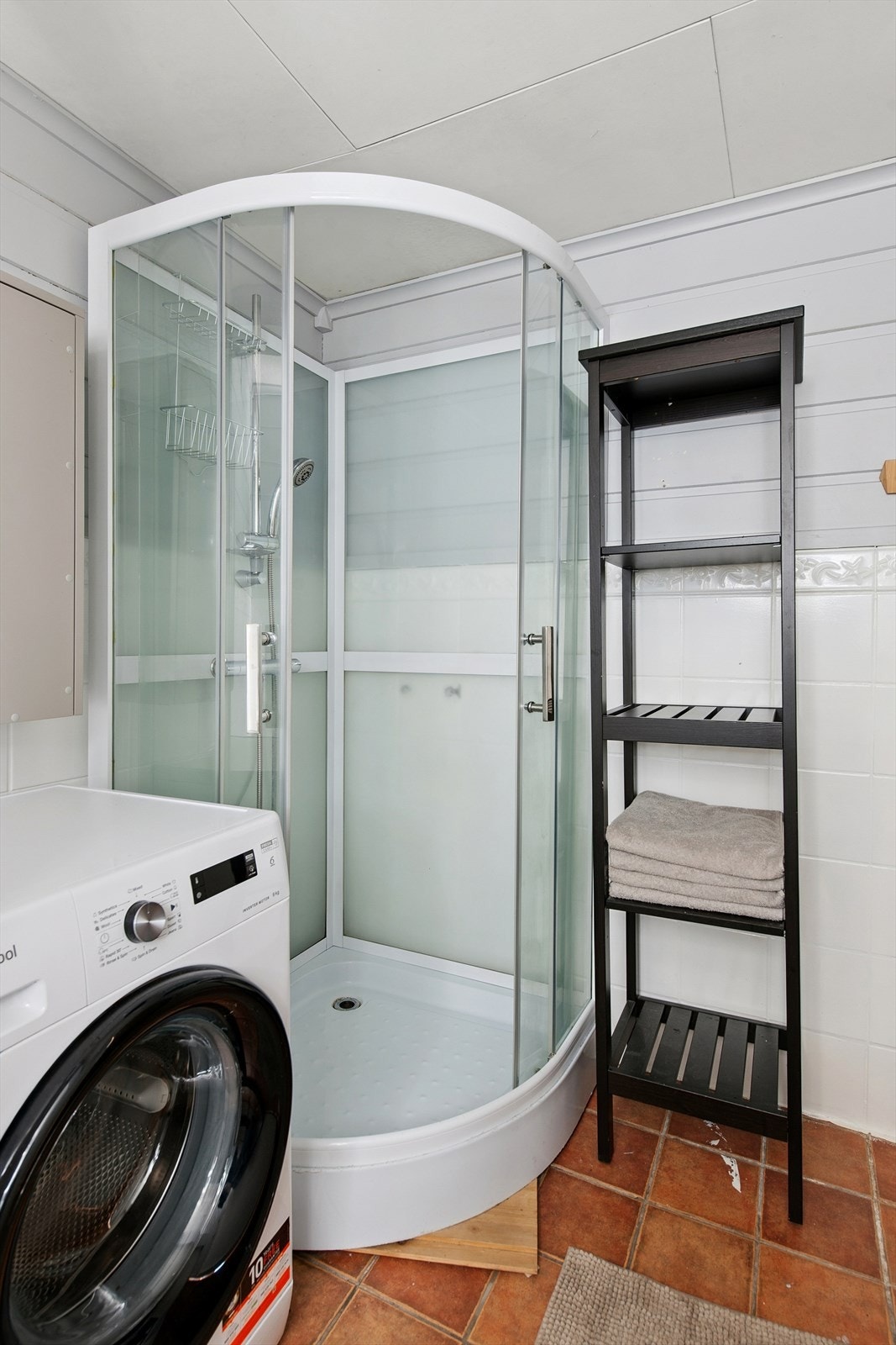 Bad med flislagt gulv, dusjkabinett, opplegg for vaskemaskin, servant og toalett. Galleribilde