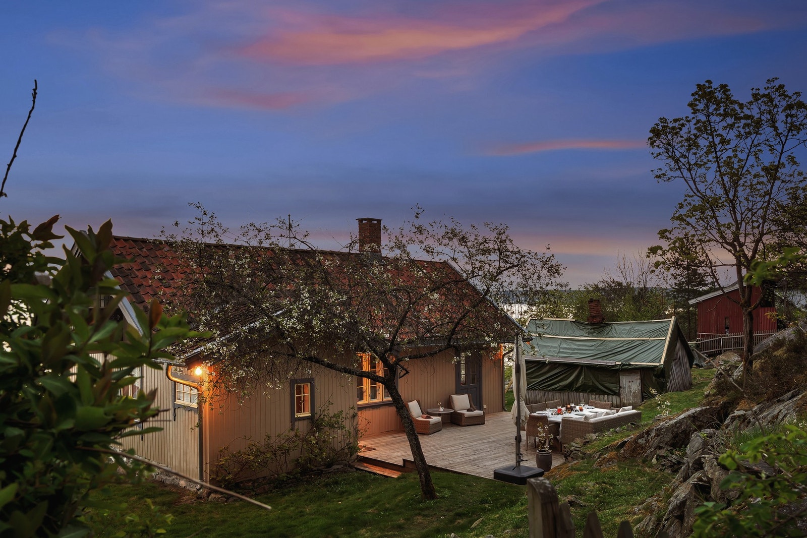 Kveldens lune stemning senker seg over eiendommen - med blomstrende trær utendørs soner som inviterer til avslapning og samvær. Galleribilde