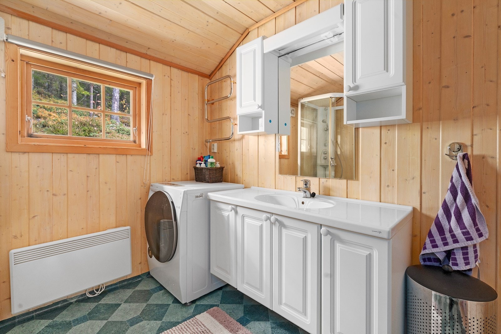 Badet har skapinnredning med nedfelt servant, overhengende speil med belysning, dusjkabinett i hjørnet, gulvstående toalett og opplegg til vaskemaskin. Galleribilde