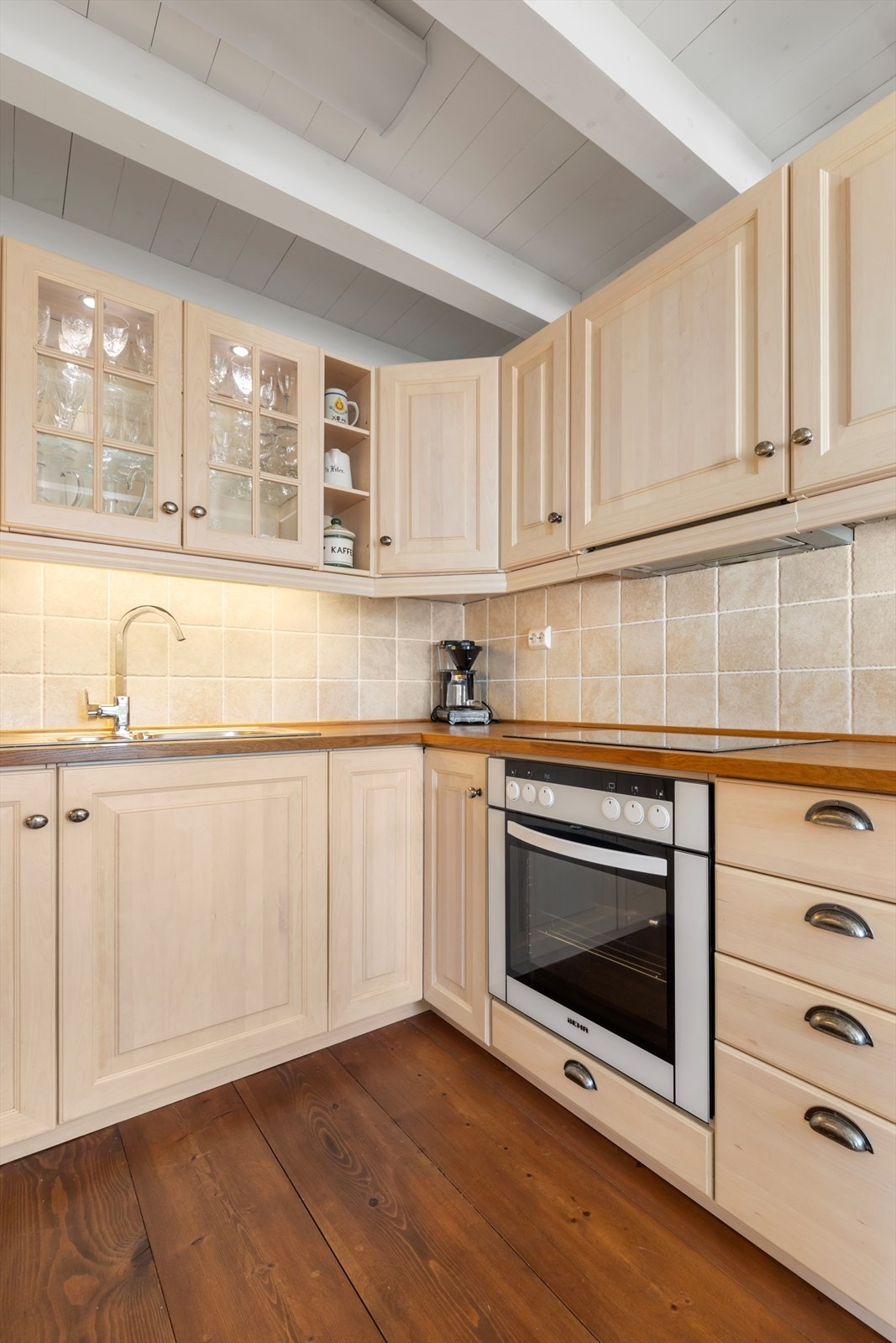 Kjøkkeninnredning med profilerte, lakka skapfronter og med glass | benkeplater av tre med nedfelt vask og platetopp | innredningen er utstyrt med integrert stekeovn og kjøleskap, og det er utsparing for oppvaskmaskin Galleribilde