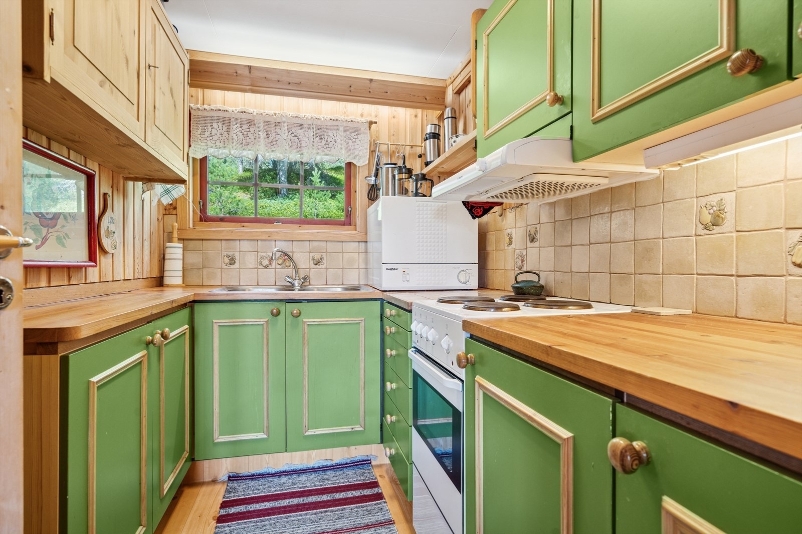 Videre i boligen ligger kjøkkenet i eget rom fra stuen, godt utstyrt med dobbel vask, komfyr med platetopp og vifte, samt benkeoppvaskmaskin Galleribilde