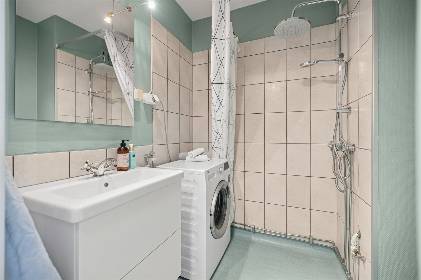 Badet har vask med underskuffer, uttak til vaskemaskin og veggmontert dusj med forheng. Toalett i rommet Galleribilde