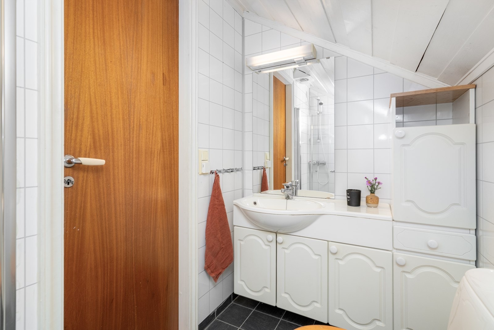 Badet inneholder servant med underskap, sideskap, speil, gulvmontert toalett og dusjhjørne. Galleribilde