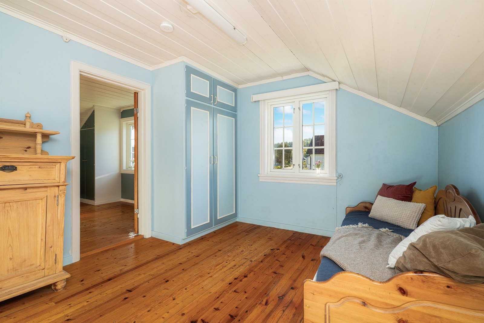 Soverom med overflater bestående av lakkert furugulv og malt panel i himling. Galleribilde