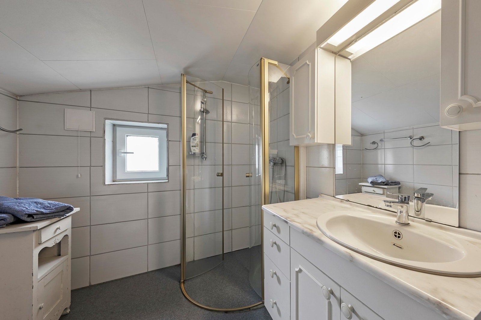 Bad i kårleilighet har baderomsinnredning og speil, dusjhjørne og gulvstående toalett. Stråleovn på vegg Galleribilde