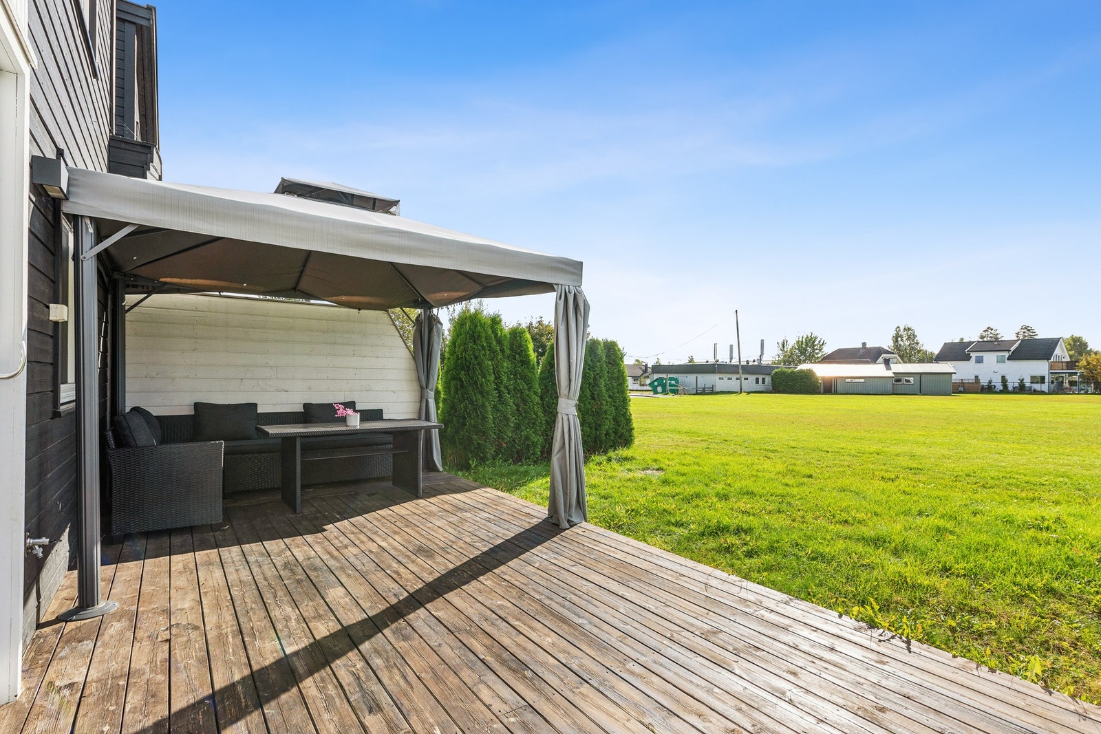 Uteplassen vender ut mot et åpent grøntområde skjermet med hekkebusker på hver sin side. Galleribilde