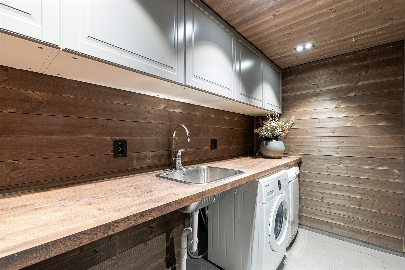 Romsleg vaskerom med mykje oppbevaring. Benkeplate i tre, med plass til vaskemaskin og tørketrommel. Galleribilde