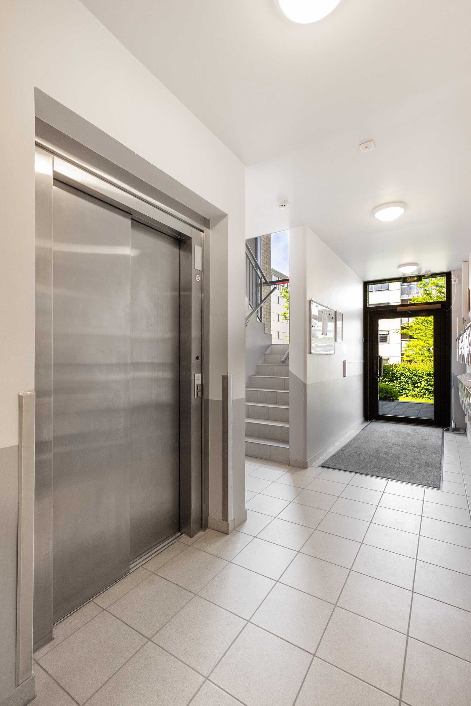 Hovedinngang på plan 0/bakkenivå med heis og trapp opp til leiligheten som ligger i 1.etasjen. Galleribilde