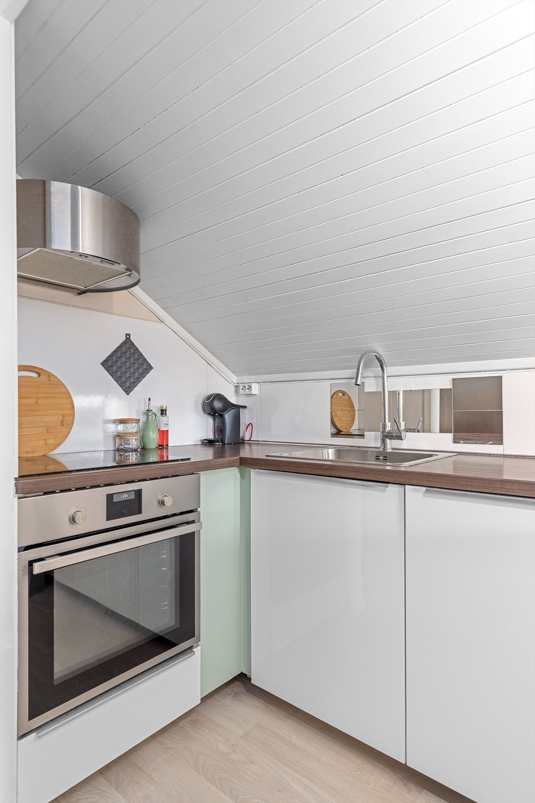 Lys innredning med integrert stekeovn, platetopp, oppvaskmaskin og frittstående kjøleskap plassert under benk Galleribilde