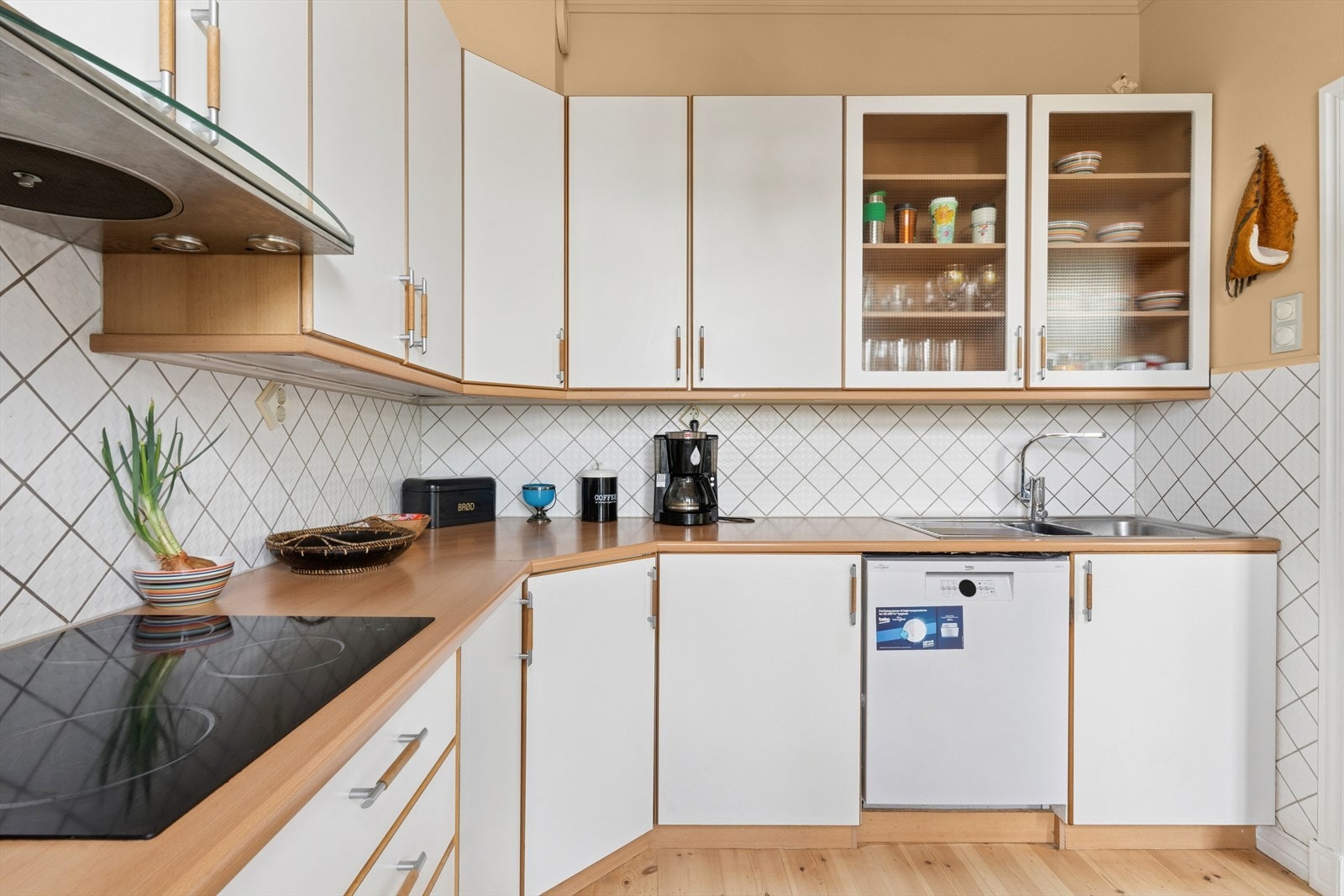 Kjøkkeninnredning med hvite glatte fronter, laminat benkeplate med nedfelt oppvaskkum, fliser på vegg over benk, kjøkkenventilator, integrert komfyr, mikro, oppvaskmaskin og kombiskap. Galleribilde