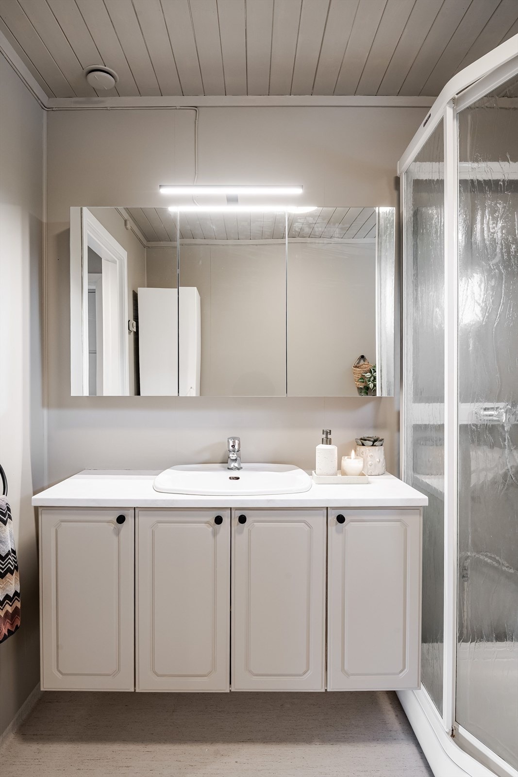 Baderommet varmes opp med panelovn og er innredet med dusjkabinett, servant på innredning og speilskap med belysning over. Galleribilde