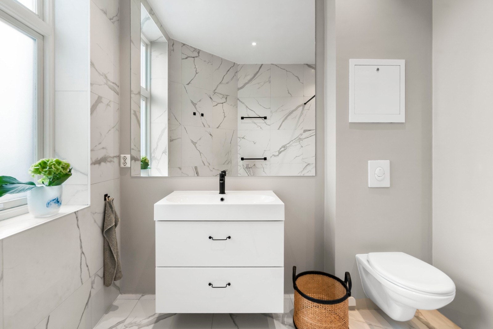 Innbydende baderomsinnredning med stort speil over servant, samt veggmontert klosett som gir et rent og tidløst preg. Galleribilde